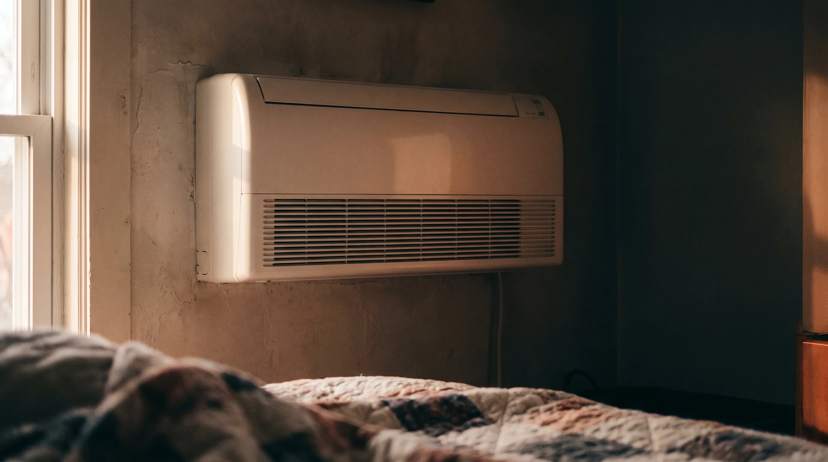 Wall-mounted ductless mini split indoor head high on a bedroom wall, the quiet half of the system