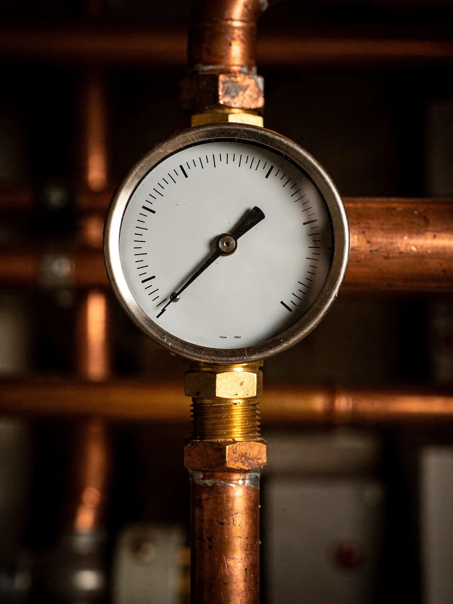 Close view of a brass pressure and temperature gauge on a boiler, copper piping soft in the background