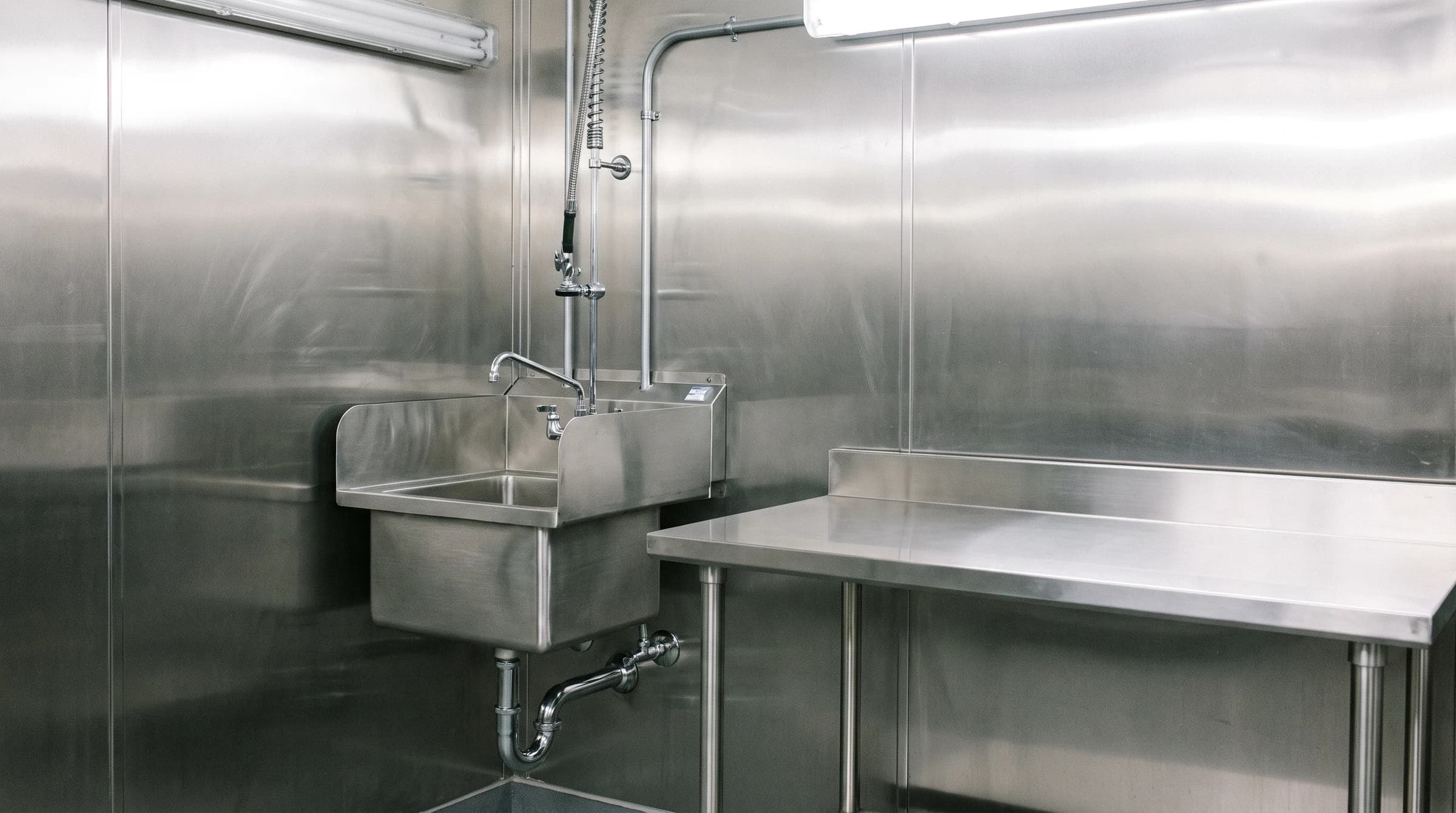 Stainless hand sink and prep table plumbed against stainless wall panels in a production space